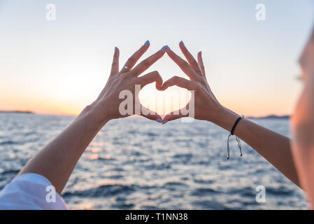Junge weibliche schöne Hände auf dem Hintergrund des Meeres zeigen das Symbol des Herzens. Ferienhäuser - Konzept. Stockfoto