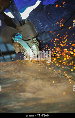 Arbeiter in der Handschuhe und Overalls schneidet Blech Winkelschleifer. Funkenflug von der Festplatte. Industrielle Hintergrund mit kopieren. Stockfoto