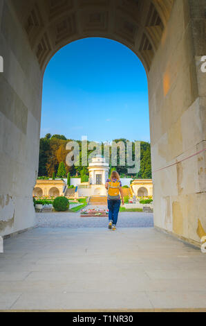 Lemberg, Ukraine - 31. August 2018: lychakiv Friedhof bei Sonnenuntergang. Junge Frau Tourist mit einem gelben Rucksack geht unter dem Bogen Stockfoto