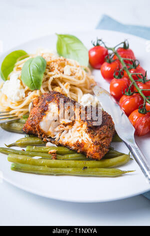 Nahaufnahme der geschwärzten Kabeljau mit grünen Bohnen, Tomaten und Nudeln. Essen und Schneiden gewürzten Fisch auf einem weißen Teller geschwärzt. Stockfoto