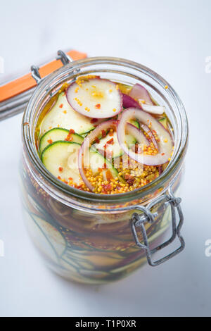 Nahaufnahme von eingelegtem zuchinni Vorspeise und Starter mit roten Zwiebeln, Gewürzen und einem vingar Beizen marinade in einer offenen Mason jar mit einem weißen Hintergrund. Stockfoto