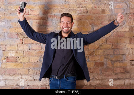 Ein glücklicher hübscher junger Geschäftsmann mit seinem Smartphone in einem Anzug. Stockfoto