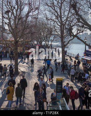 Touristen und Einheimische, die das Londoner Spaziergang entlang der Themse an der South Bank in der Nähe des London Eye und die warmen Sonnenstrahlen an einem Nachmittag Ende März genießen. Stockfoto