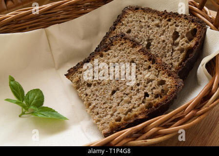 Hausgemachtes Schwarzbrot Scheiben mit grünem Basilikum in einem Weidenkorb, Country Stil. Stockfoto