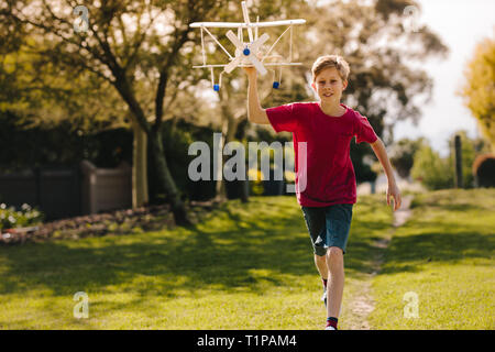 Glückliche junge spielt mit einem Spielzeug Flugzeug in den Park. Begeistert junge läuft mit einem Spielzeug Flugzeug im Freien. Stockfoto