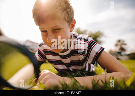 Junge durch die Lupe an einem sonnigen Tag. Kaukasischen jungen erkunden Garten mit seiner Lupe. Stockfoto