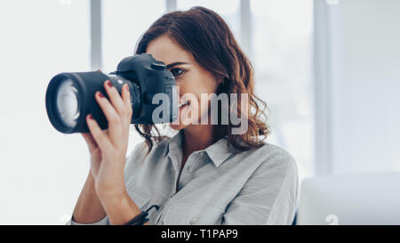 Frau mit DSLR-Kamera in Innenräumen fotografieren. Kaukasische Fotografin mit der Kamera Bilder aufnehmen. Stockfoto