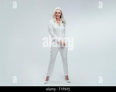 Die ganze Länge der Attraktive, reife Frau, die auf weißen Hintergrund. Schöne ältere Frau posiert in Weiß casuals. Stockfoto