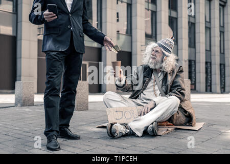 Lächelnde grauhaarige schmutzig Arbeitslose Mann sitzt auf dem Boden Stockfoto