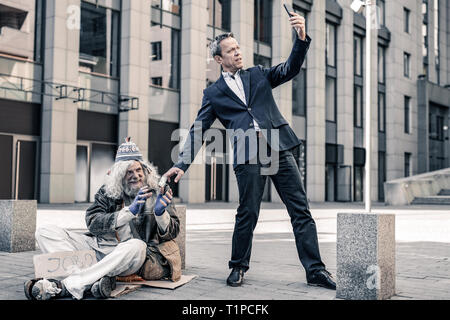 Kommunikative alte obdachlose Sitzen auf kalten Boden mit Papier Schale Stockfoto