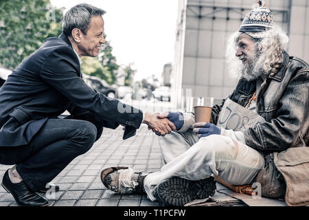 Neugierig kurzhaarige Geschäftsmann sitzen vor der langhaarigen Obdachlose Stockfoto
