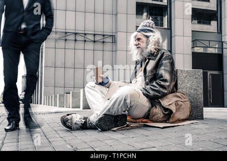 Miserable grauhaarige alte obdachlose regungslos sitzen auf kalten Boden Stockfoto