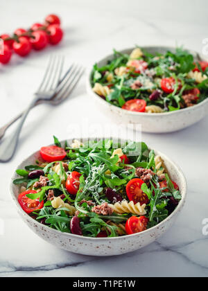 Warmer Salat mit Thunfisch, Rucola, Tomaten, rote Bohne, Pasta. Idee und Rezept für gesundes Mittag- oder Abendessen. zwei Schüsseln mit warmen Salaten auf Marmortisch. Ideen und Rezepte für gesundes Mittag- oder Abendessen. Vertikale Stockfoto