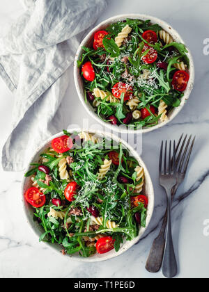 Warmer Salat mit Thunfisch, Rucola, Tomaten, rote Bohne, Pasta. Idee und Rezept für gesundes Mittag- oder Abendessen. zwei Schüsseln mit warmen Salaten auf Marmortisch. Ideen und Rezepte für gesundes Mittag- oder Abendessen. Vertikale Stockfoto