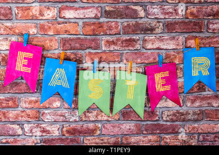 Bunte handgemachte Flags mit lsekf gemalte Buchstaben, Beschriftung Ostern, rote Ziegel Wand Hintergrund. Stockfoto