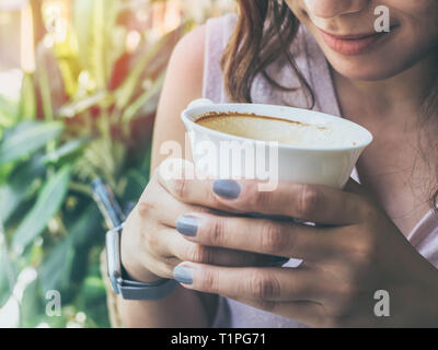 Close-up Frau Hände halten einen weißen heißen Kaffee Tasse und duftenden Kaffee auf grüne Natur Hintergrund. Stockfoto