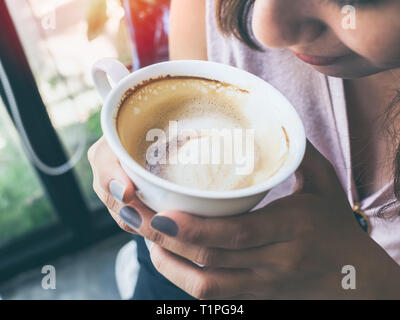 Close-up Frau Hände halten einen weißen heißen Kaffee Tasse und duftenden Kaffee auf grüne Natur Hintergrund. Stockfoto