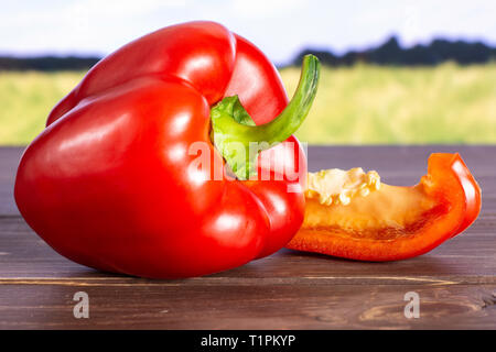 Gruppe von einer ganzen Scheibe des bulgarischen Roten Paprika mit grünen Weizenfeld im Hintergrund Stockfoto