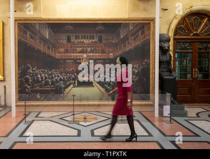 Ein Passant auf dem Gemälde "Das Parlament entwickelt" durch die Graffiti Künstler Banksy, der auf der Bristol Museum ist. Stockfoto