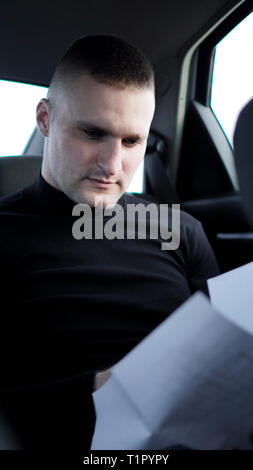 Junge Unternehmer auf der Suche durch Dokumente, während an der Rückseite eines Auto sitzen Stockfoto