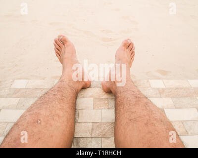 Mann ist entspannend barfuß am Strand. Nahaufnahme Beine haut Asien Mann und Männer behaarte Beine auf Sand Hintergrund. Guy's Beine in den Sand. Stockfoto