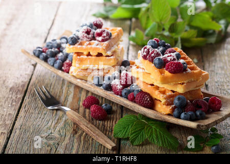 Waffeln mit Himbeeren und Blaubeeren auf einem alten Holztisch. Stockfoto