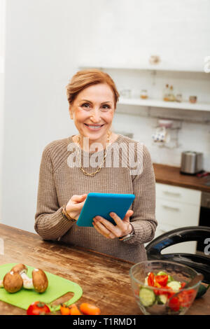 Freudige attraktive Frau in der Nähe von Holz- Tisch und Kontrolle der Medien Stockfoto