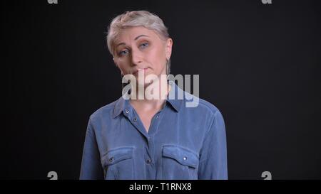 Closeup Portrait von Erwachsenen attraktive kaukasischen Frauen mit kurzen blonden Haaren an Kamera mit Hintergrund auf Schwarz auf der Suche Stockfoto