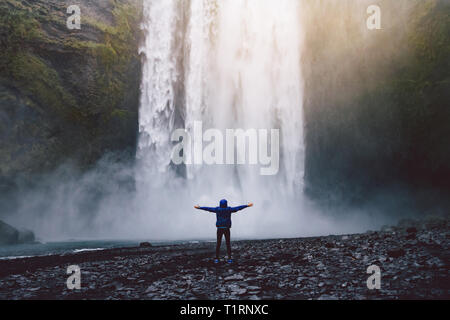 Eine Person admirnig die Schönheit der Skogafoss Wasserfall in Island entfernt Stockfoto