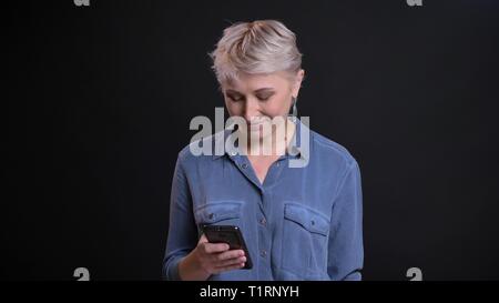 Closeup Portrait von Erwachsenen kaukasischen Frauen mit kurzen blonden Haaren SMS am Telefon vor der Kamera Stockfoto