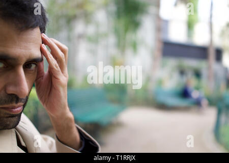 Schöner Mann der pakistanische, indische, asiatische Herkunft, im City Park sitzen, Hand, Kopf Stockfoto