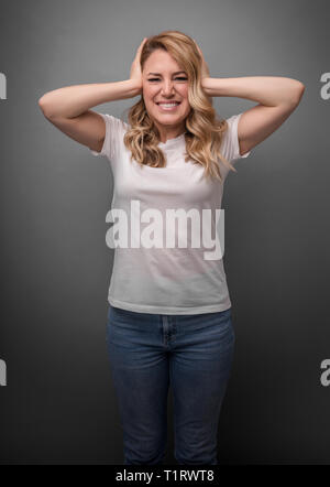 Attraktive Frau deckt Ihre Ohren mit den Händen auf einem grauen Hintergrund. Stockfoto