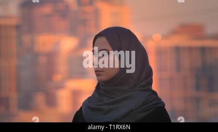 Closeup Seitenansicht Porträt der jungen attraktiven weiblichen im hijab direkt von der Kamera mit der Stadt im Hintergrund. Stockfoto
