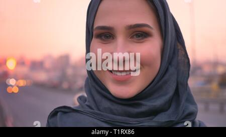 Closeup Schießen der jungen attraktiven weiblichen Gesicht im hijab direkt an der Kamera und lächelnd mit städtischen Umgebung auf dem Hintergrund Stockfoto