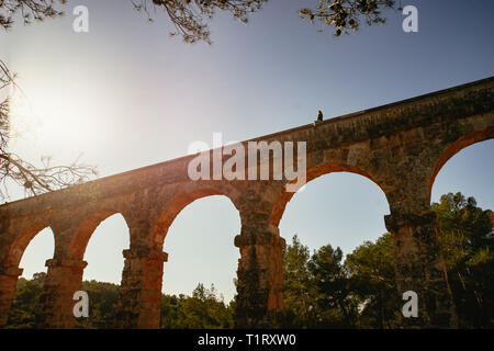 Römisches Aquädukt Pont del Diable in Tarragona, Spanien. Rebellische junge Frau sitzt auf der Spitze des Denkmals. Stockfoto
