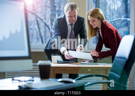Geschäftspartner diskutieren bei der Besprechung über Dokumente und Ideen. Mann und Frau in Anzügen arbeiten mit Papieren rund um den Tisch im Büro. Arbeitsbereich Stockfoto