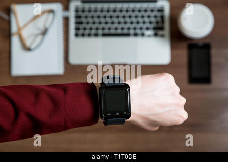 Business Person, die am Schreibtisch arbeitet, Laptop tippt und verwendet, Draufsicht. Smart Watch auf dem Tisch und Smartphone auf dem Tisch. Kaffeetasse, Notizblock und g Stockfoto