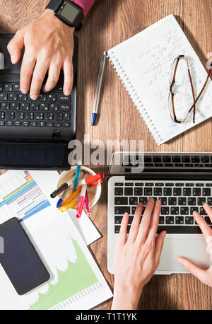 Zwei Personen im Büro Schreibtisch arbeiten, schreiben und mit Laptop, Ansicht von oben, flach. Smart Watch an Hand und Smart Phone auf dem Tisch. Kaffeetasse Stockfoto