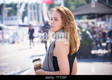 Portrait von lächelnden stilvolle Frau mittleren Alters entlang Meer Bucht. Segelboote im Hafen, Meer. Sommertag. Wind im Haar, trinken Kaffee Stockfoto