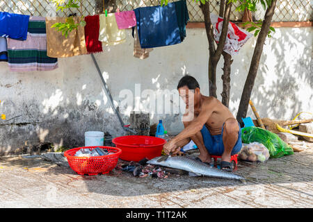 Lokaler Mann schneiden und Ausnehmen eines frisch gefangenen Fisch, mit einem Holzklotz und ein Messer, auf dem Bürgersteig, Dinh Cau Dorf, Phu Quoc, Vietnam, Asien Stockfoto