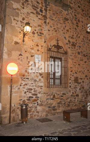 Fassade aus Stein mit Lampe, vergitterten Fenster, Sitzbank und Transit Zeichen in der Dämmerung in Caceres. Ein Dorf voll von alten Gebäuden in Spanien. Stockfoto