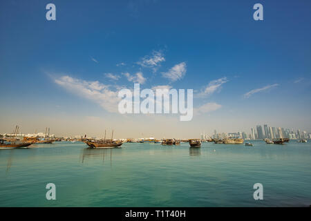 Die hölzernen Dhow Boote in Doha Hafen und den zahlreichen Wolkenkratzern, mit hellen Morgen Haze, in Al Dafna Viertel und auf dem Hintergrund gesehen, Q Stockfoto