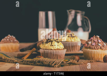 Hausgemachte Muffins Cupcakes mit Schokolade und Vanille Creme auf einem Holzbrett mit einem Glas Milch in background-image Stockfoto