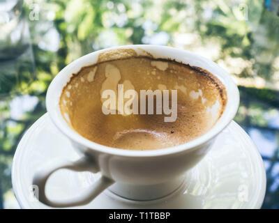Blick von oben auf die leeren heißen Kaffee in weisser Keramik Schale nach Trinken auf Glas Tisch mit Blick in die Natur die Reflexion. Stockfoto