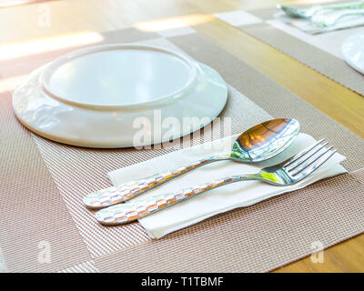 Close-up weiße Platte mit Edelstahl Löffel und Gabel auf der Platte Matte auf Holztisch. Stockfoto