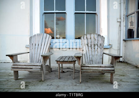 Zwei hölzernen Sessel auf einem Deck vor ein viktorianisches Haus mit blau lackierten Windows; gesehen in Tintagel, Cornwall (UK) Stockfoto