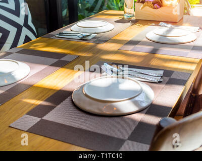 Weiße Platten, Edelstahl, Löffel und Gabeln auf Platte Matten mit Blumenstrauß lila Blumen auf Holztisch. Esstisch im Restaurant in der Nähe von Glas wi einstellen Stockfoto