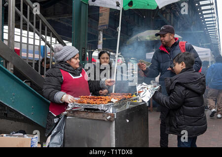 Eine Südamerikanische Frau verkaufen Gegrilltes Fleisch aus einem Stand unterhalb der erhöhten und U-Bahn. In der Corona, Queens, NYC Stockfoto