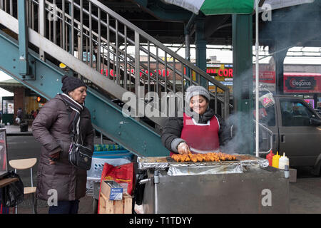 Eine Südamerikanische Frau verkaufen Gegrilltes Fleisch aus einem Stand unterhalb der erhöhten und U-Bahn. In der Corona, Queens, NYC Stockfoto