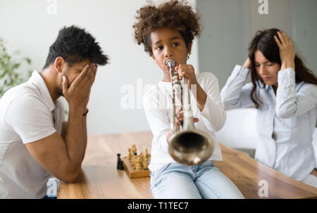 Mutter und Vater versucht, Schach zu spielen, während ihr Kind spielt Trompete Stockfoto